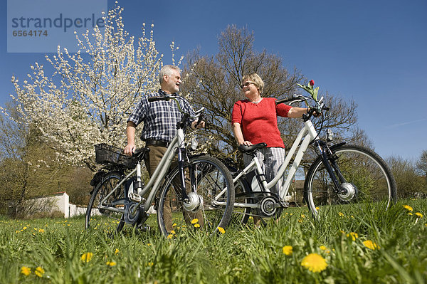 Germany  Bavaria  Senior couple standing with electric bicycle on meadow
