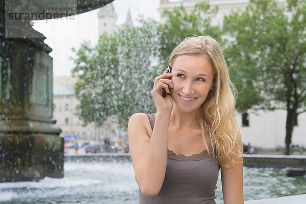 Junge Frau am Telefon vor der Ludwig-Maximilians-Universität lächelnd