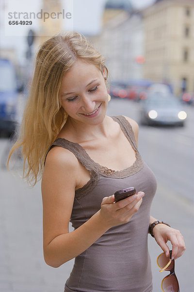 Young woman with smart phone in front ofn State Library at Ludwigstrasse