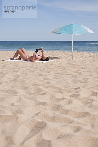 Portugal  Lagos  Mid adult woman reading book on beach