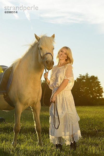 Lächelnde Frau in weißem Kleid mit Pferd auf einer Wiese