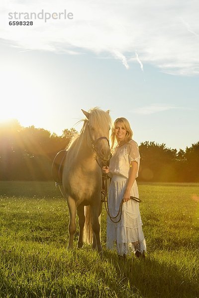 Lächelnde Frau in weißem Kleid mit Pferd auf einer Wiese