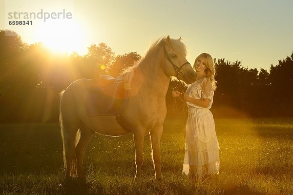 Lächelnde Frau in weißem Kleid mit Pferd auf einer Wiese