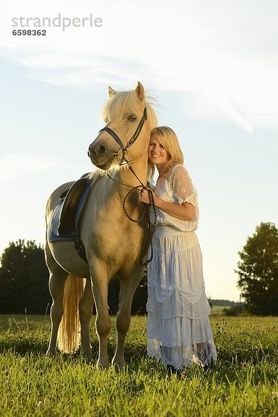 Lächelnde Frau in weißem Kleid mit Pferd auf einer Wiese