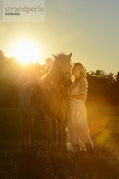 Lächelnde Frau in weißem Kleid mit Pferd auf einer Wiese