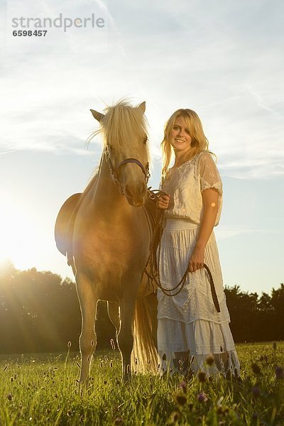 Lächelnde Frau in weißem Kleid mit Pferd auf einer Wiese