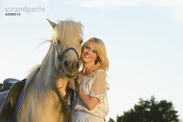 Lächelnde Frau in weißem Kleid mit Pferd  Portrait