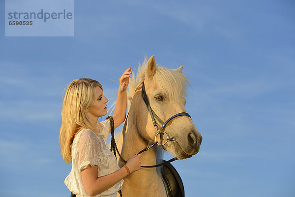 Junge Frau in weißem Kleid mit Pferd unter blauem Himmel