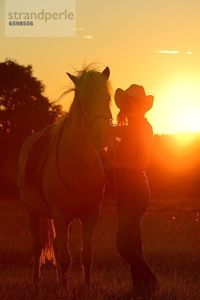 Junge Frau mit Pferd auf einer Wiese im Gegenlicht