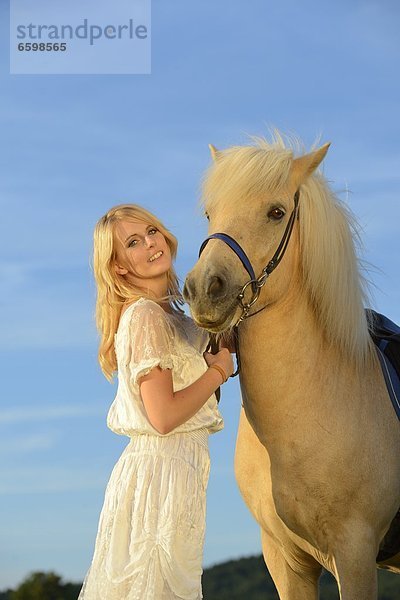 Lächelnde Frau in weißem Kleid mit Pferd unter blauem Himmel