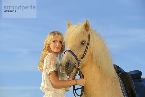 Lächelnde Frau in weißem Kleid mit Pferd unter blauem Himmel