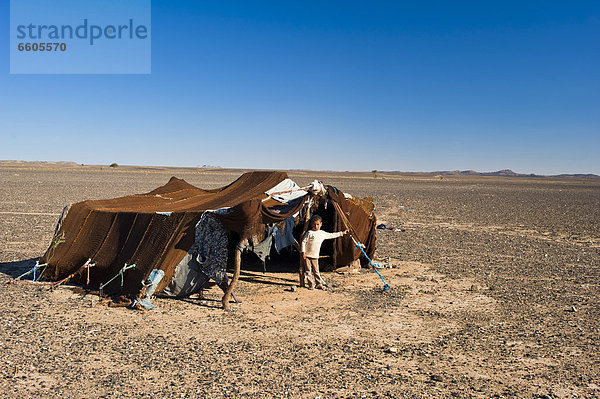 Ein kleiner Junge steht vor dem Wohnzelt seiner Nomadenfamilie  Steinwüste  Hammada  Erg Chebbi  Südmarokko  Marokko  Afrika