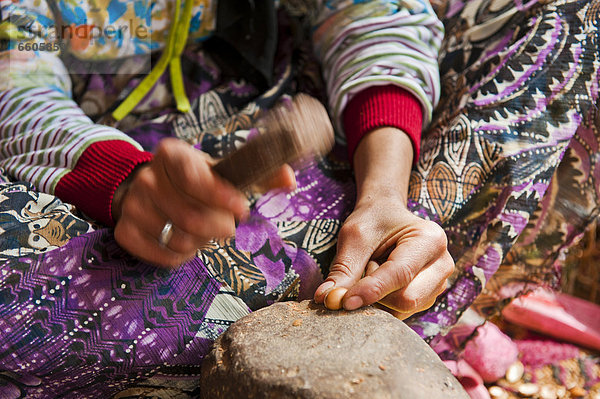 Eine Berberfrau schlägt mit einem Stein auf einem Steinamboss Argannüsse auf  um die Kerne für die Zubereitung von Arganöl herauszulösen  Antiatlas  Südmarokko  Marokko  Afrika