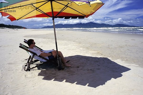 sitzend  Mann  Strand  Regenschirm  Schirm  unterhalb  Liege  Liegen  Liegestuhl  Seitenansicht  Sonnenschirm  Schirm