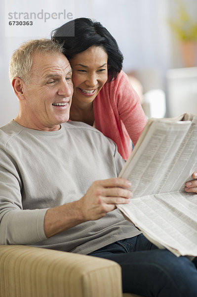 Mature couple sitting in armchair  reading newspaper