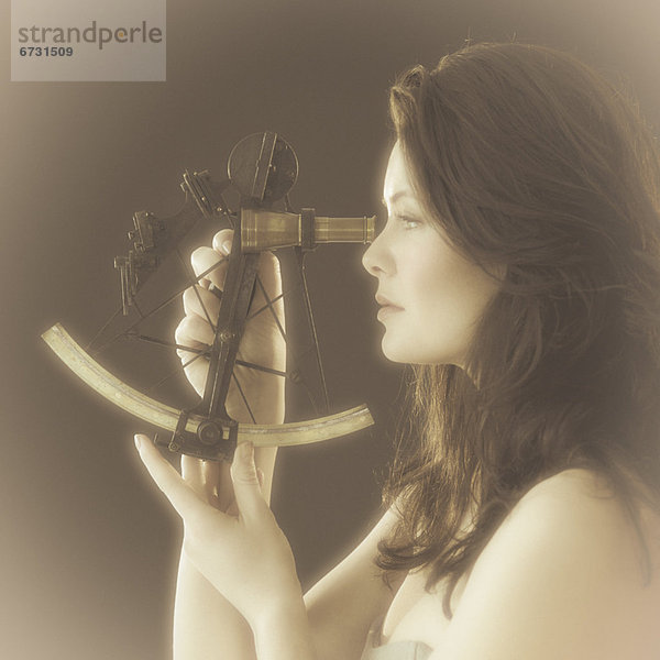 Woman looking through antique sextant  world map in background