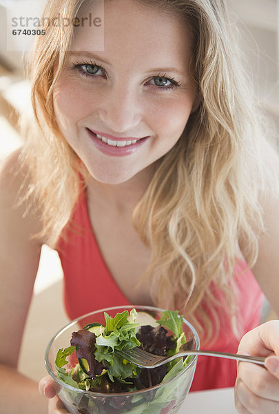 Junge Frau isst stehend einen Salat