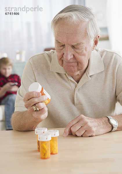 Grandfather holding pill bottle  grandson (8-9) in background