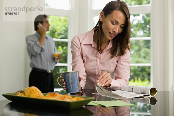 Woman Reading  Man on Cellphone in Kitchen