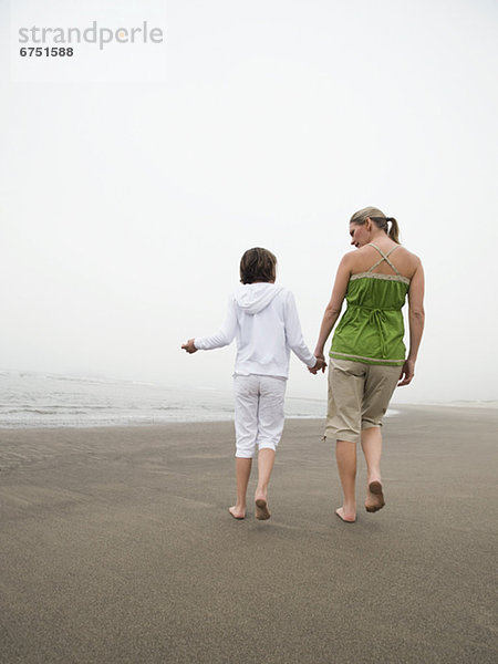 Mutter und Tochter halten Händchen und laufen am Strand
