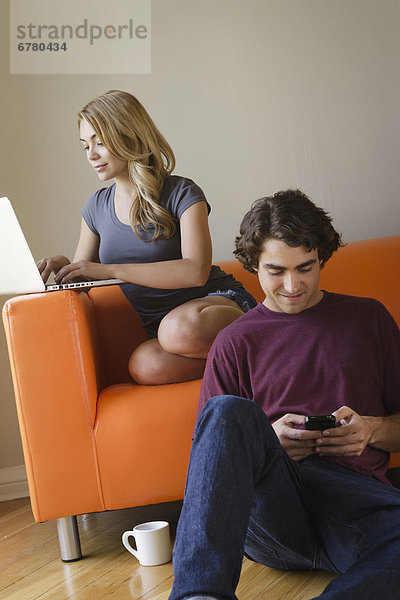 Young couple in living room  using phone and laptop