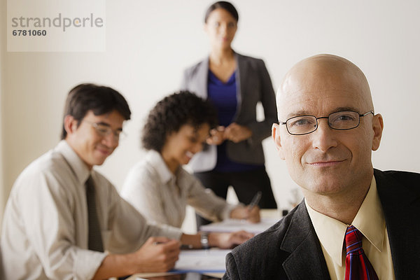 Mature businessman looking at camera  business team in background