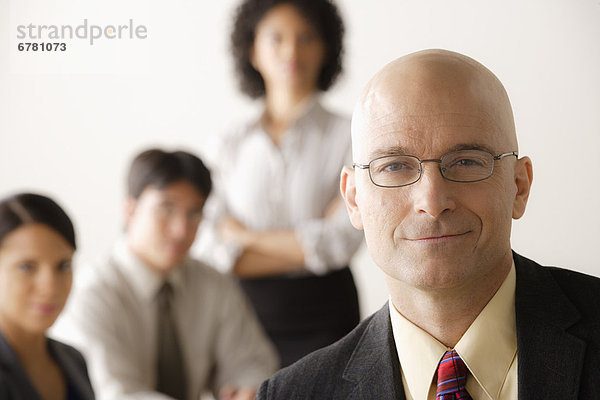 Mature businessman looking at camera  business team in background
