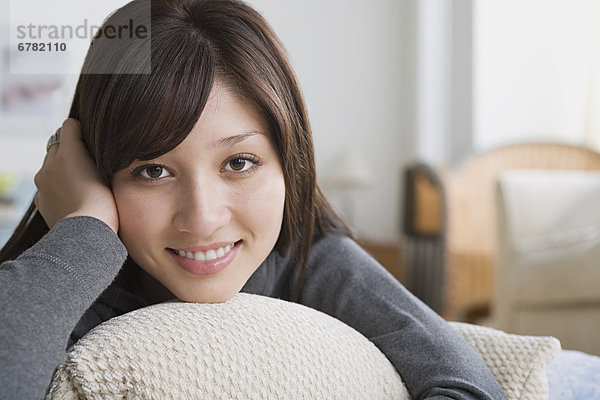 Junge Frau liegt auf Sofa  Kopf auf Händen  lacht in Kamera  Porträt