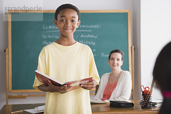 Schoolboy posing with book  teacher in background