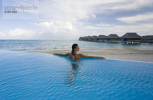 French Polynesia  Moorea  Woman relaxing in resort pool  Luxury resort bungalows in background.