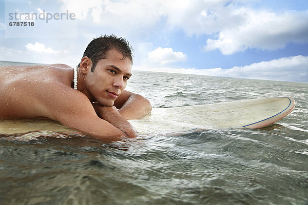 Hawaii  Oahu  junger Mann sitzt auf seinem Surfbrett im Wasser.