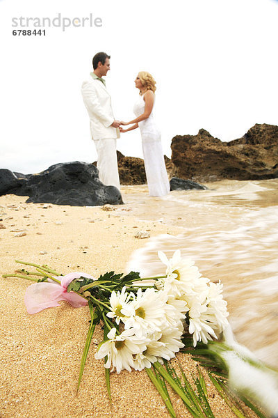 Hawaii  Oahu  Latina Hochzeitspaar hält und suchen in einander mit Bouquet von weißen Daisies im Vordergrund wird gewaschen durch das Meer am Strand