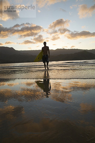 Hawaii  Kauai  Hanalei Bay  junger Mann am Strand zu Fuß mit Surfboard bei Sonnenuntergang.
