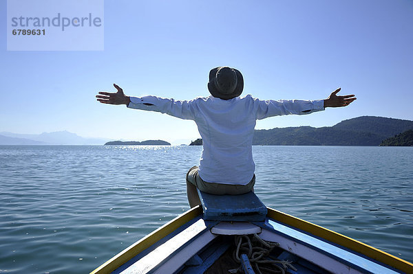 Junger Mann mit weit geöffneten Armen am Bug eines Fischerbootes  Paraty oder Parati  Bundesstaat Rio de Janeiro  Brasilien  Südamerika