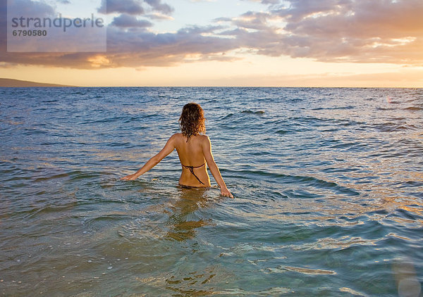 Hawaii  Kauai  Frau zu Fuß in den Ozean als die Sonne-Sets.