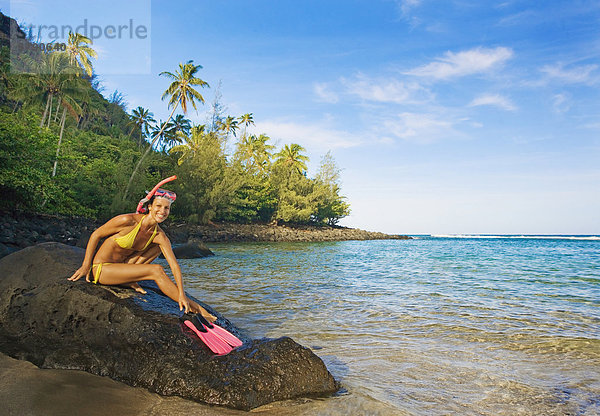 Hawaii  Kauai  Kee Beach  Frau mit Schnorchel Ausrüstung lächelnd auf einem Felsen. Schnorchelausrüstung