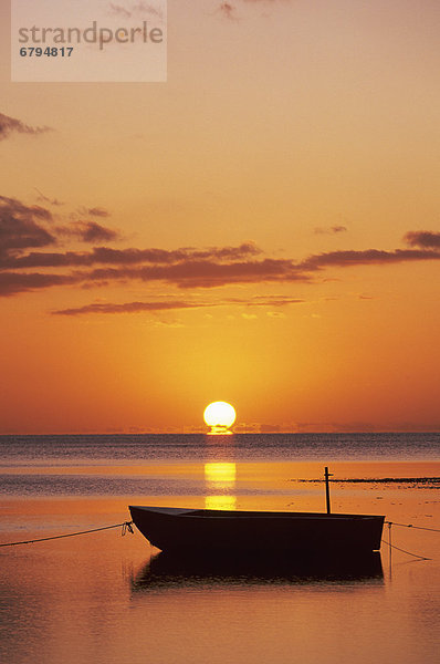 Sun setting over ocean  Boat silhouetted against orange sky.