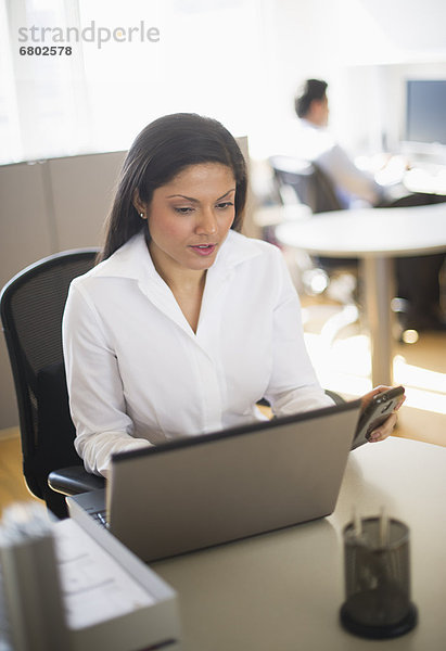 Businesswoman working on laptop  businessman in background