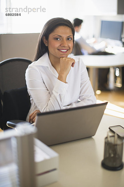 Businesswoman working on laptop  businessman in background