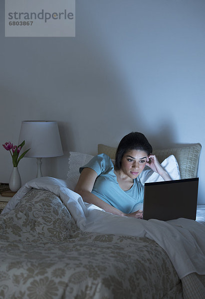 Junge Frau mit Laptop im Bett