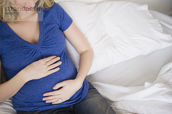 Schwangere Frau sitzt im Bett