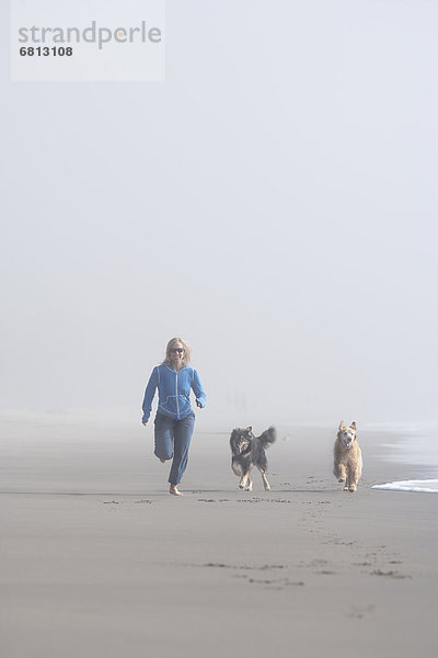 nebeneinander  neben  Seite an Seite  Frau  Strand  rennen  Hund  Nebel  Sand