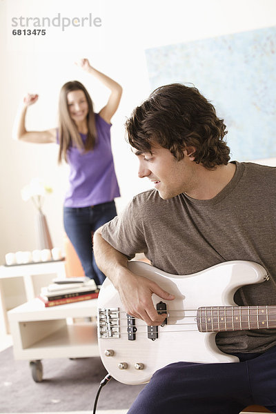 Young man playing electric guitar  young woman dancing in background
