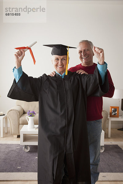 Senior woman wearing graduation gown  happy man in background