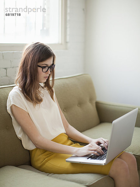 Junge Frau sitzend auf Sofa mit laptop