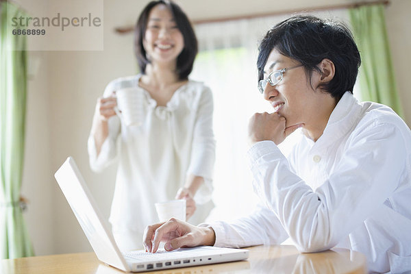 Young Man Using Laptop  Girlfriend in Background