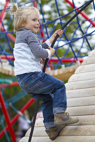 Blondes Mädchen klettert auf einem Spielplatz