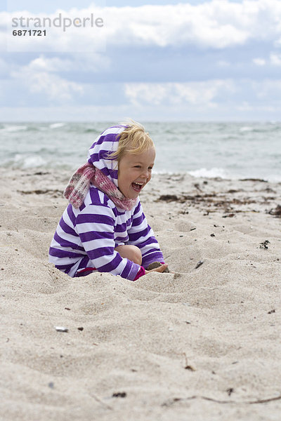 Fröhliches Mädchen spielt im Sand am Strand
