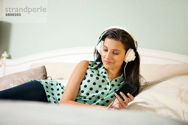 Junge Frau im Bett mit Kopfhörern