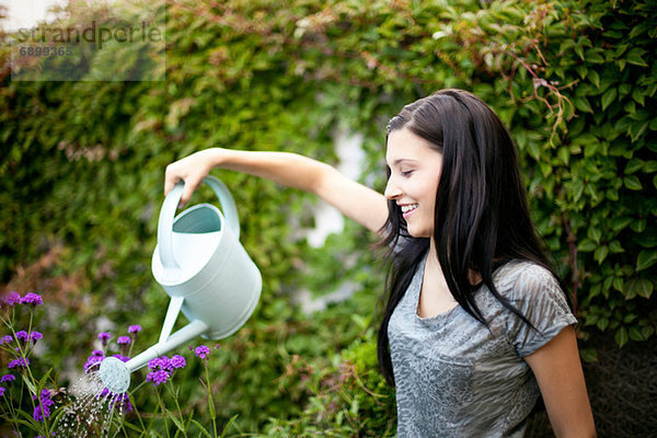Junge Frau gießt Blumen im Garten